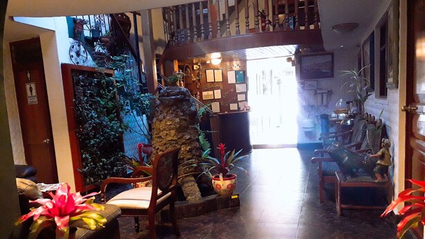 A lobby with a stone column, wooden furniture, and potted plants. - Hostal Santa Apolonia (Cajamarca)