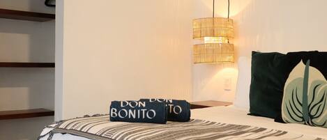 Una cama bien hecha con una colcha a rayas y almohadas, una lámpara colgante y un estante con estructura de madera.