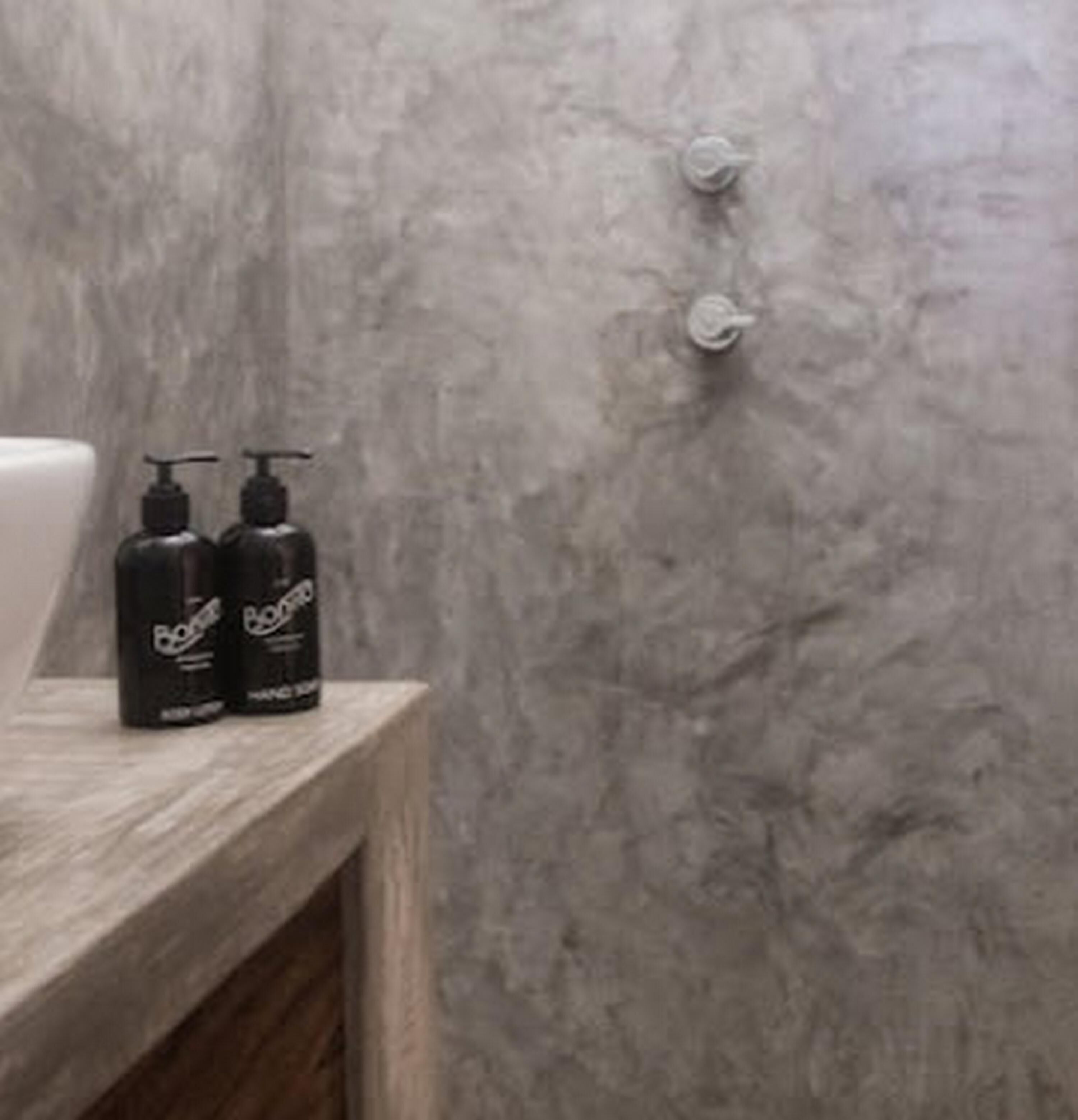 Un baño con pared de mármol, tocador de madera y dos botellas de Champú Bena.