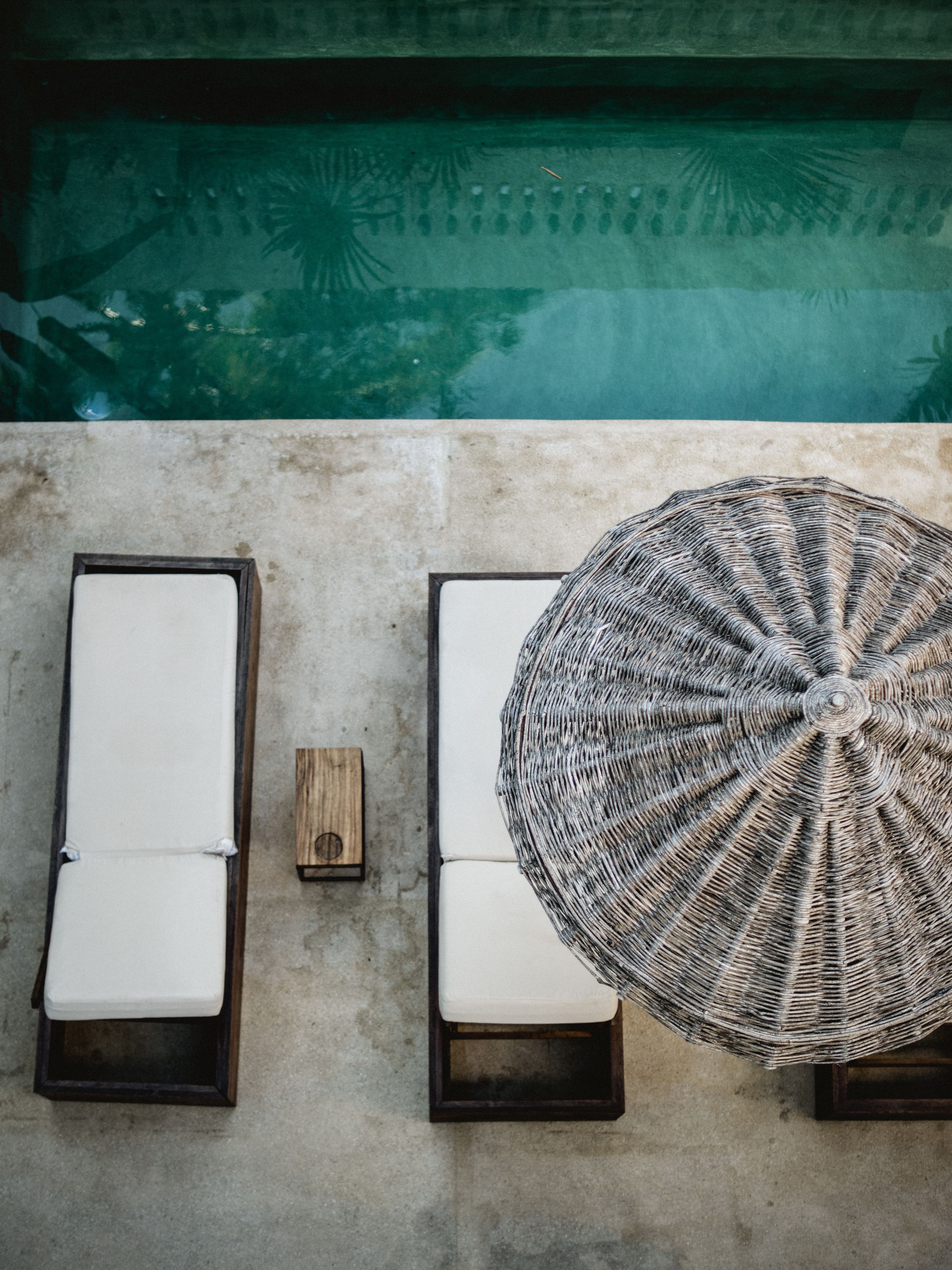 Zona de piscina con dos sillas de descanso y una sombrilla tejida.