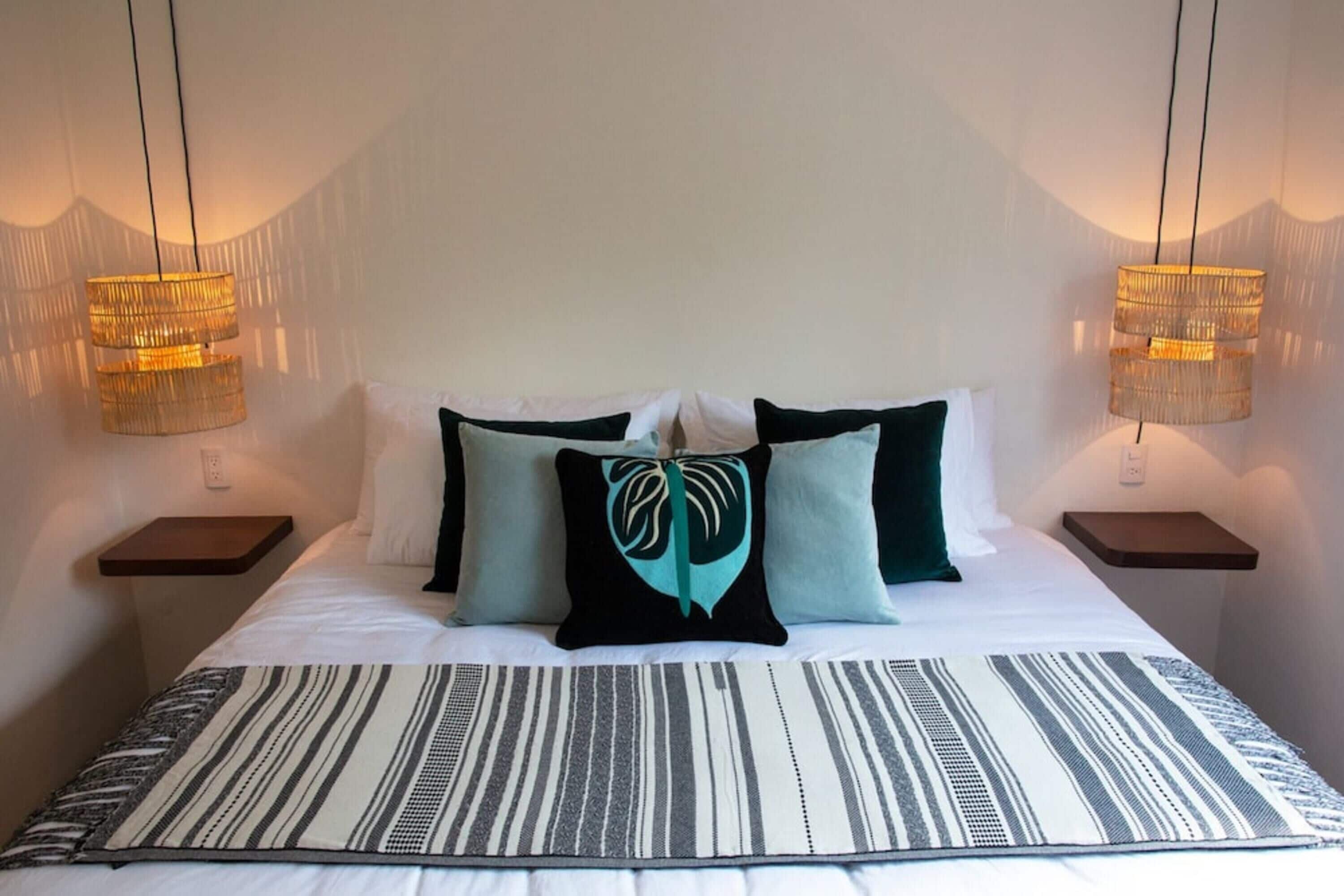 Una cama bien hecha con un edredón a rayas, dos mesitas de noche con lámparas y una almohada con diseño de hojas.