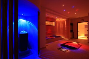 Un espace bien-être comprenant un bassin illuminé de lumière bleue, un sauna et une salle de massage.