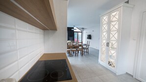 A modern kitchen with a black induction cooktop, wooden cabinets, and a dining area with a table and chairs. - Dom nad jeziorem (gmina Rogowo)