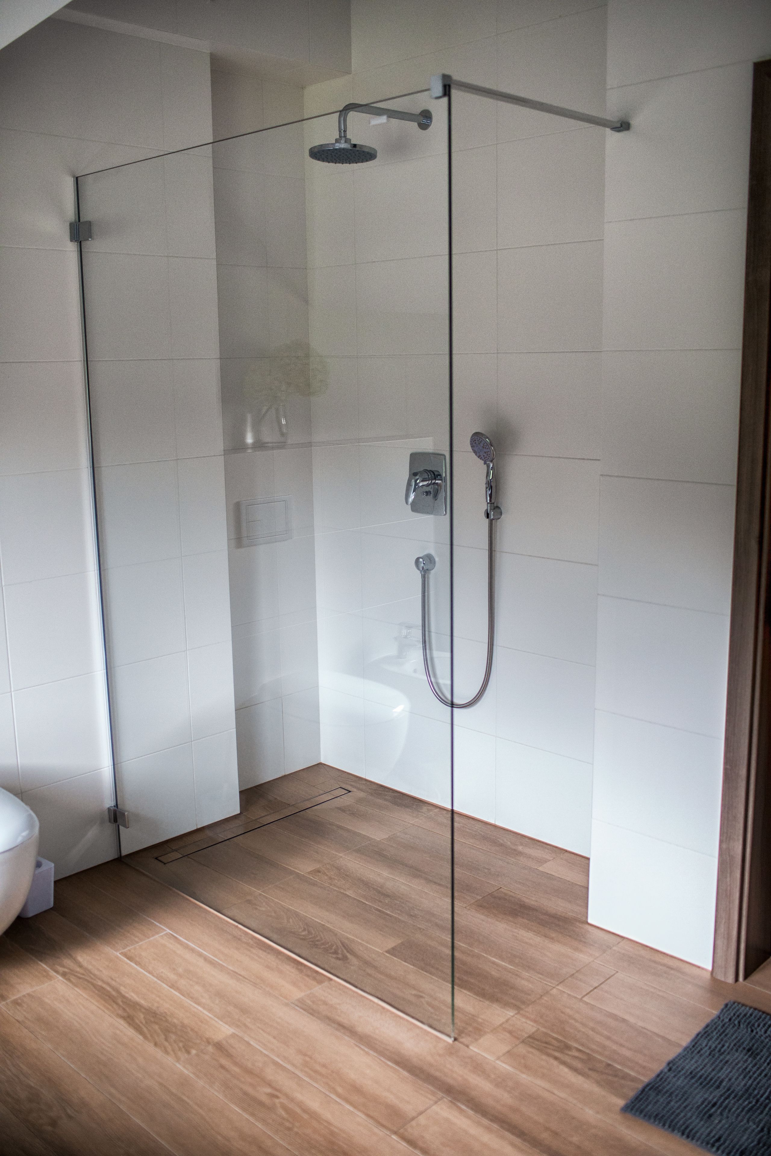 Een douchecabine met glazen wanden, een handdouche en een wandmengkraan.