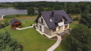 A modern two-story house with a dark roof, a covered porch, and a small wooden cabin. - Dom nad jeziorem (gmina Rogowo)
