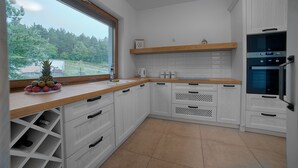 A modern kitchen with white cabinetry, a wooden countertop, and a view of a forest through a large window. - Dom nad jeziorem (gmina Rogowo)