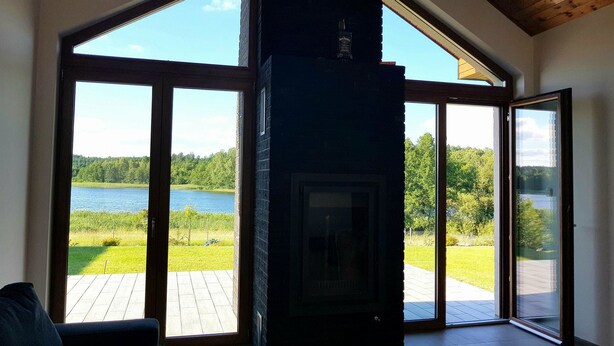 A room with a fireplace, large windows, and a view of a lake. - Dom nad jeziorem (gmina Rogowo)