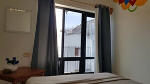 A bedroom with a bed, a small table, a vase with flowers, and a window with curtains. - Hostel Vallarta - Adults only (Puerto Vallarta)