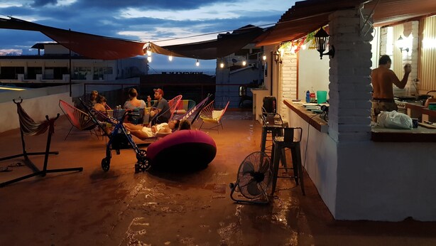 A rooftop terrace with a dining area, a fan, and a person working at a counter. - Hostel Vallarta - Adults only (Puerto Vallarta)