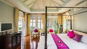 Quarto de hotel com cama, televisão, secretária e varanda com plantas.