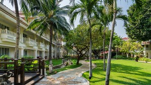 A hotel courtyard with a paved walkway, palm trees, and a decorative stone pattern. - Wora Bura Hua Hin Suite and Villa (Hua Hin)