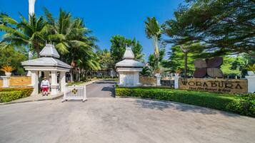 Entrada de um resort com uma placa indicando "Wora Bura Hua Hin Resort & Spa", palmeiras e céu claro.