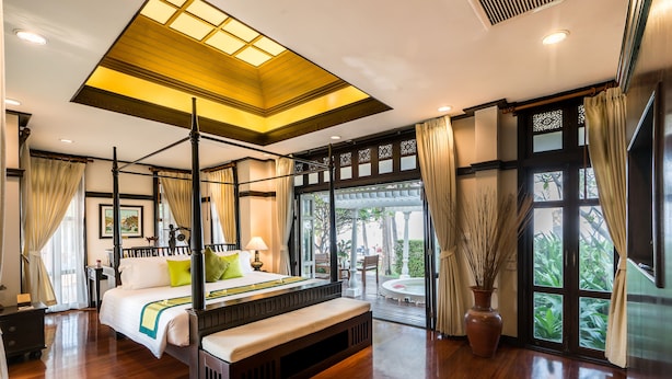 A spacious bedroom with a four-poster bed, a bench, a large window with curtains, and a view of greenery outside. - Wora Bura Hua Hin Suite and Villa (Hua Hin)