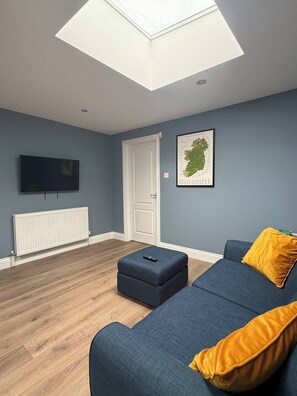A modern living room with a sofa, ottoman, and a mounted TV. - The Nook County Dublin (Shankill)