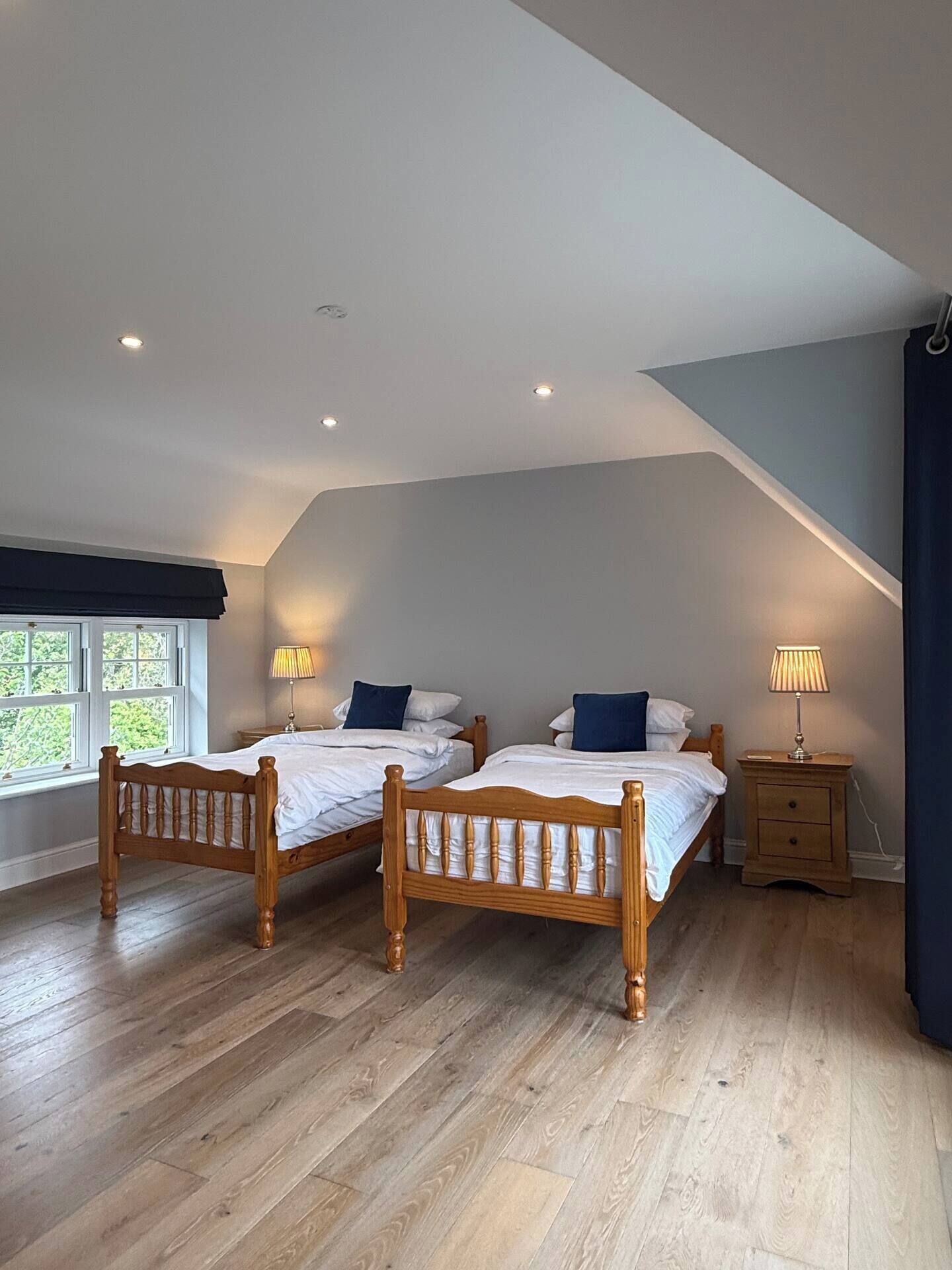A bedroom with two wooden beds, a window with a view, and a nightstand with a lamp.