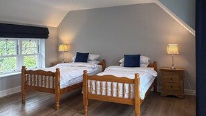 A bedroom with two wooden beds, a window with a view, and a nightstand with a lamp.
