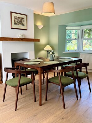 A dining area with a wooden table, green upholstered chairs, a hanging lamp, and a framed picture on the wall. - The Nook County Dublin (Shankill)