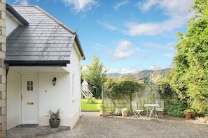 A house with a white door, a small porch, a potted plant, a wooden fence, and a view of a green landscape. - The Nook, County Dublin (Shankill)