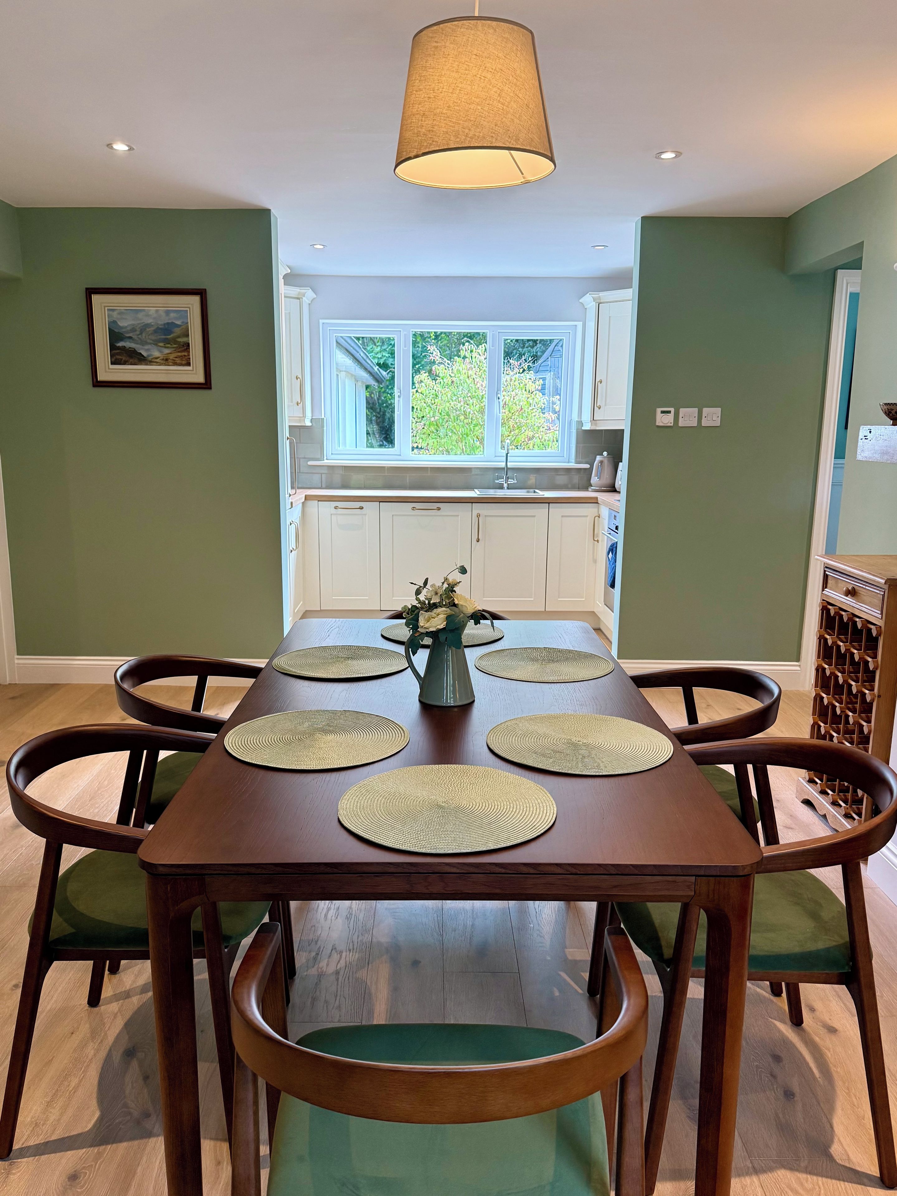 A dining area with a wooden table, green upholstered chairs, and a vase with flowers.
