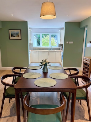 A dining area with a wooden table, green upholstered chairs, and a vase with flowers. - The Nook, County Dublin (Shankill)