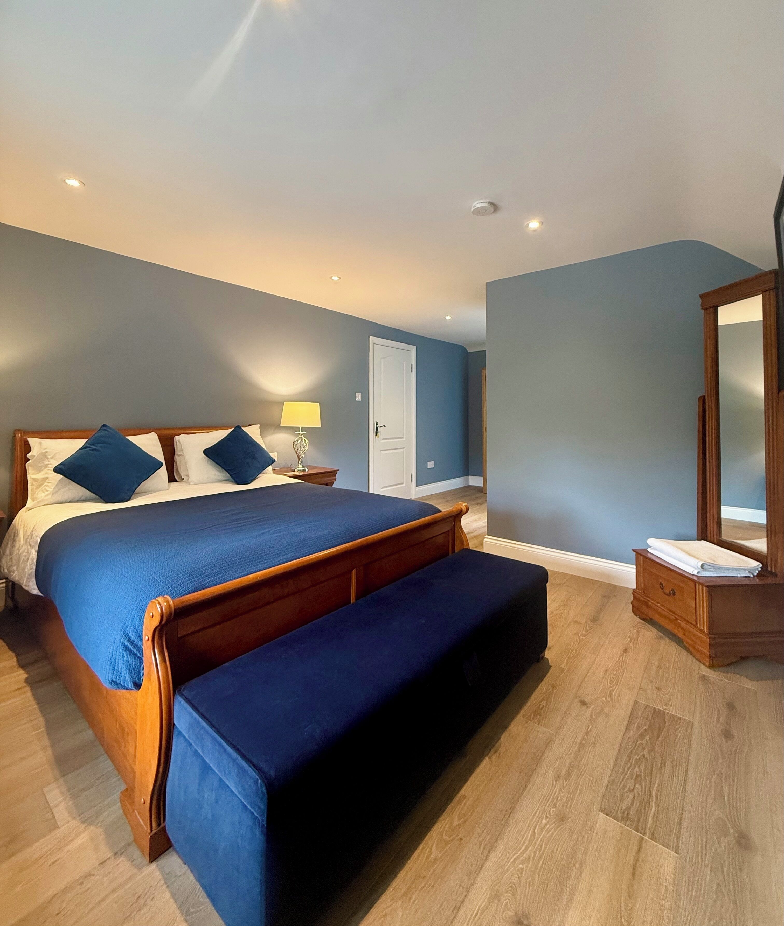 Une chambre à coucher comprenant un lit, un banc, une table de chevet, une lampe et un miroir.