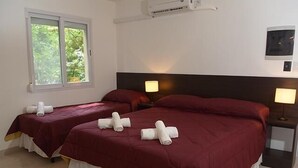 Habitación de hotel con dos camas, cada una con ropa de cama roja y almohadas blancas, una ventana con vistas a zonas verdes y un aire acondicionado de pared.