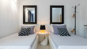 Ein Hotelzimmer mit zwei Betten, einem Nachttisch mit Lampe, einem Kleiderständer und einem Spiegel an der Wand.