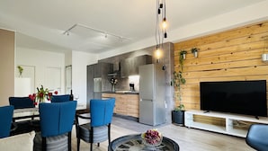 Ein modernes Wohnzimmer mit Essbereich, einer dahinterliegenden Küche und einer Wand aus Holz mit Pflanzen.