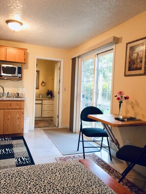 Cozy kitchen with microwave, dining area with wooden table and chairs, and a large window.
