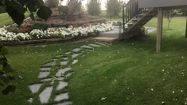 En havegang med brosten, omgivet af græs og blomsterbede.