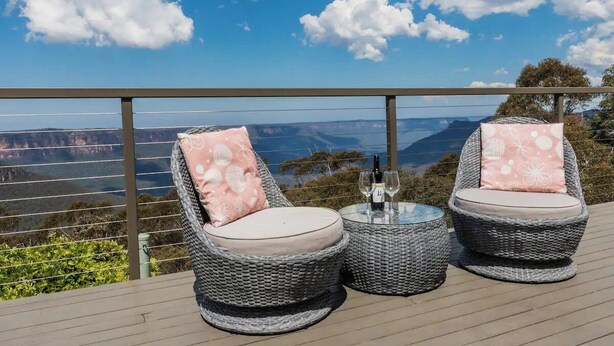 Zwei Korbstühle mit Kissen und ein kleiner Tisch mit zwei Weingläsern und einer Flasche, mit Blick auf eine reizvolle Landschaft.