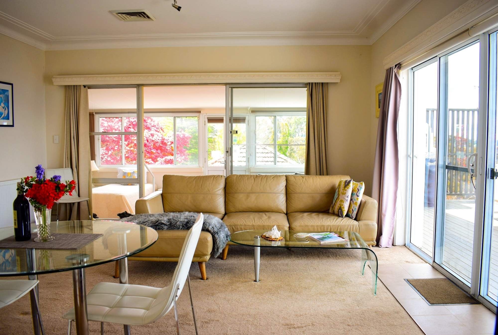 A living room with a beige sofa, a glass coffee table, and a glass dining table.