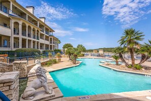 A hotel with a swimming pool, palm trees, and a stone lion statue.