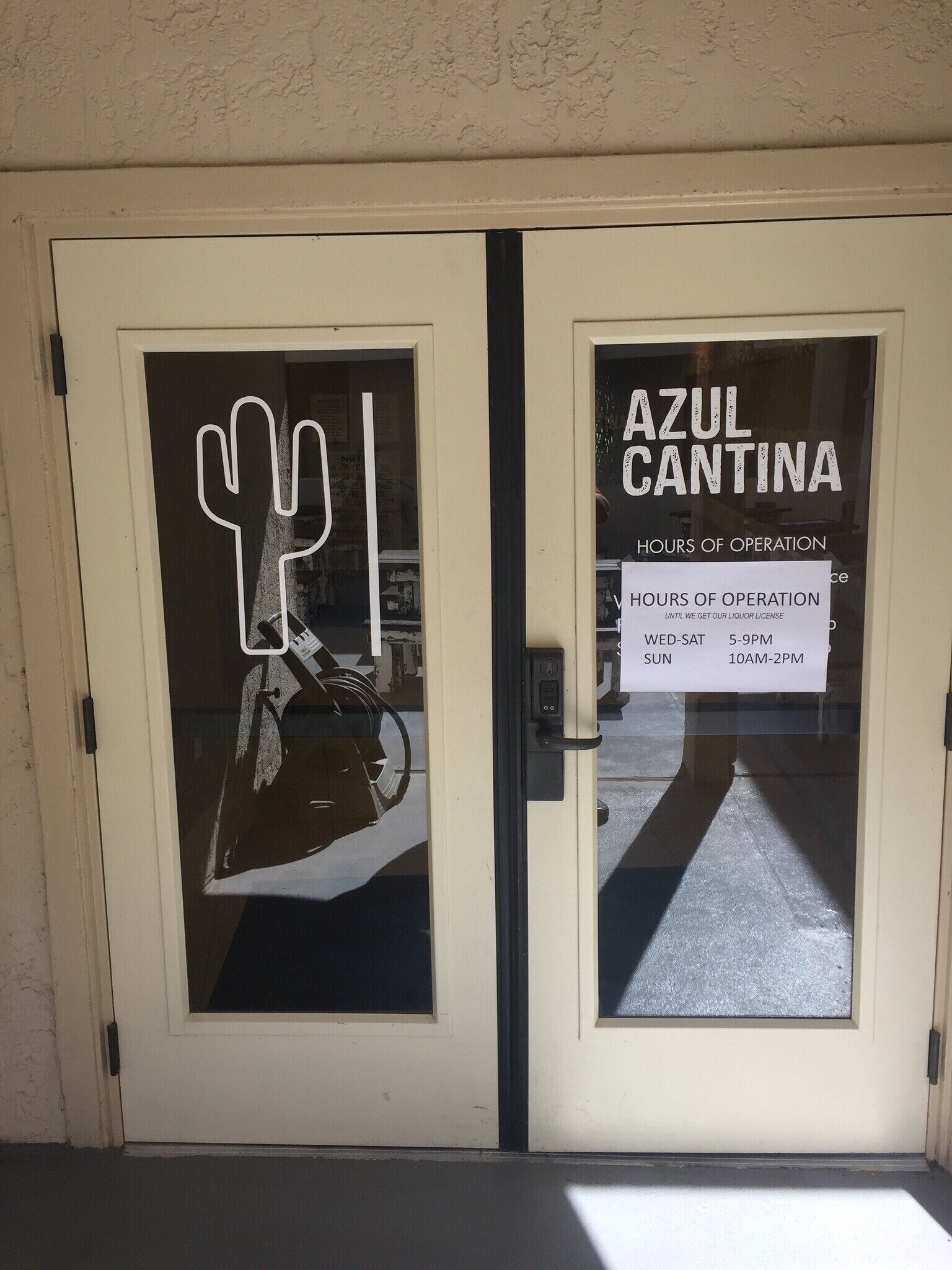 A door with a sign indicating 'AZUL CANTINA HOURS OF OPERATION' and a partial view of a cactus decoration.