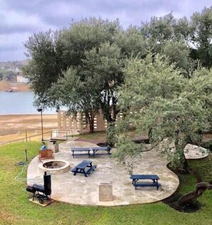 A patio area with stone flooring, picnic tables, a fire pit, and a view of a body of water.