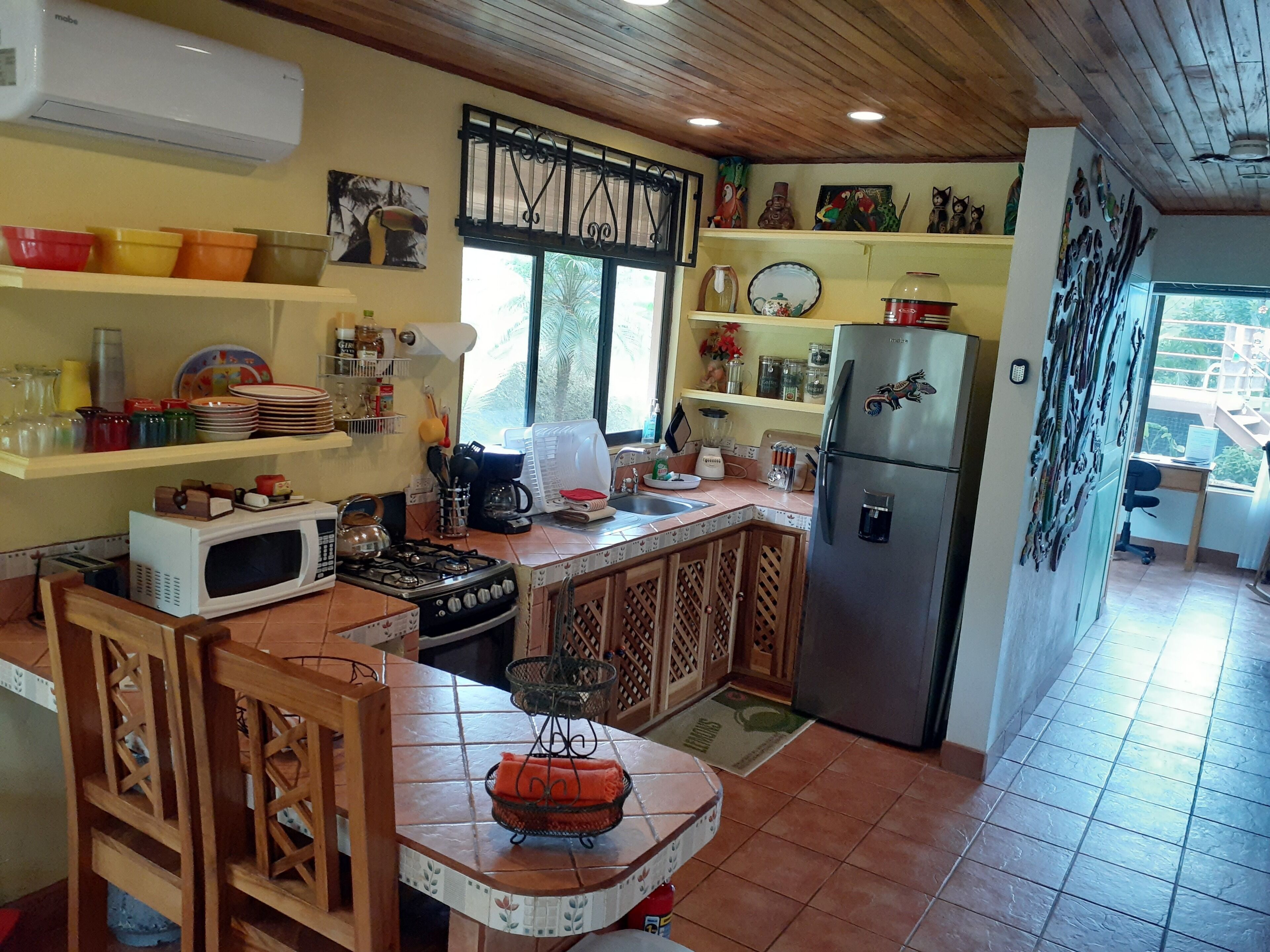 A kitchen with a stove, microwave, refrigerator, and various kitchen items on shelves.