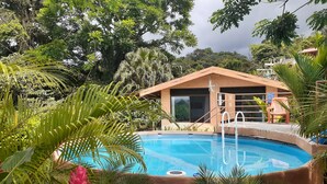 A pool area with a modern building, surrounded by lush greenery. - Romantic Hidden Jungle Gem for Two, Spectacular Views, Spa, A/C & Private Pool (El Castillo)