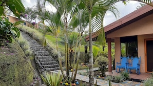 A garden with a stone staircase, palm trees, and a tiled patio area with blue chairs. - Romantic Hidden Jungle Gem for Two, Spectacular Views, Spa, A/C & Private Pool (El Castillo)