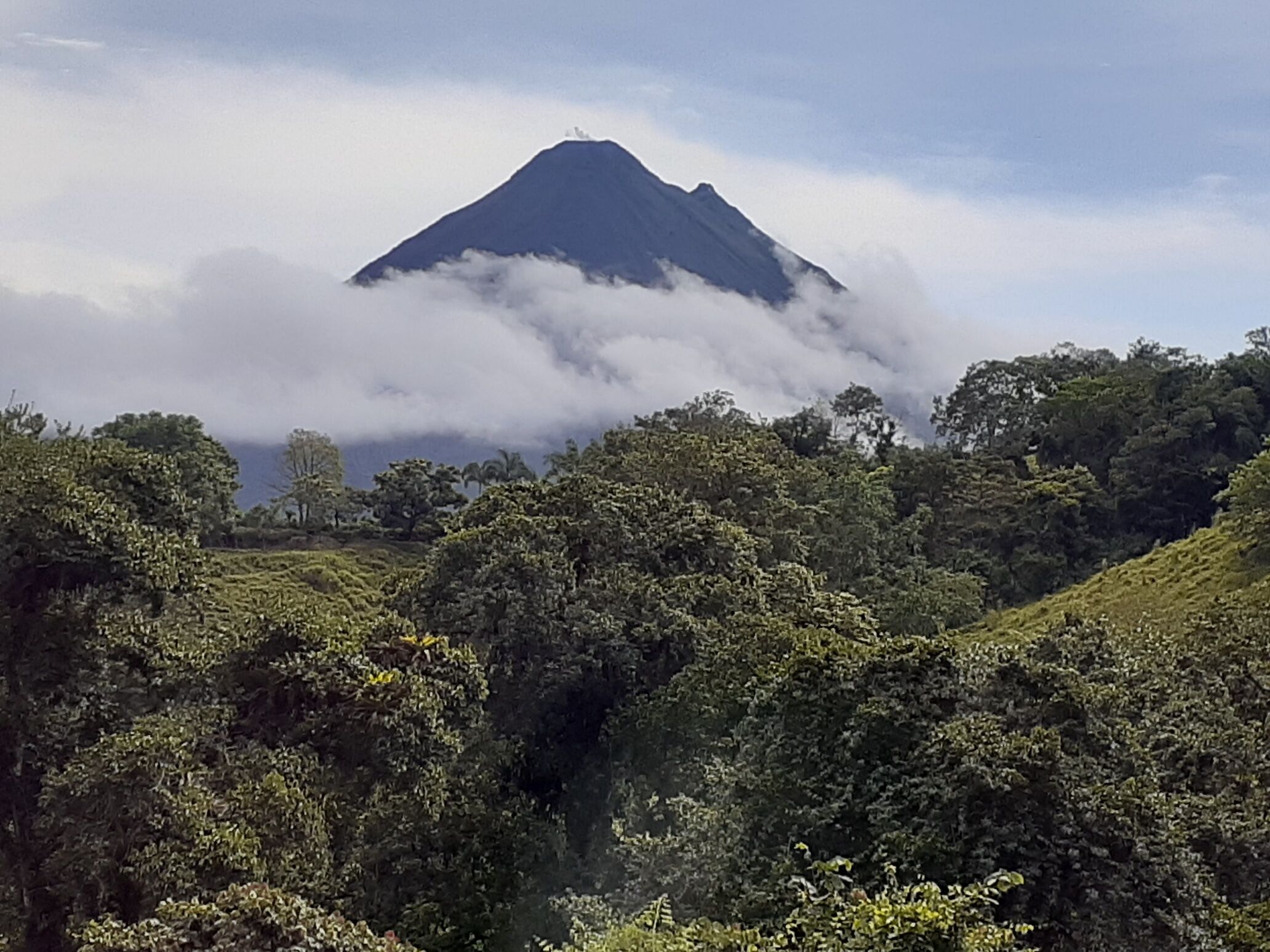 A mountain with a peak covered in clouds, surrounded by lush green vegetation.