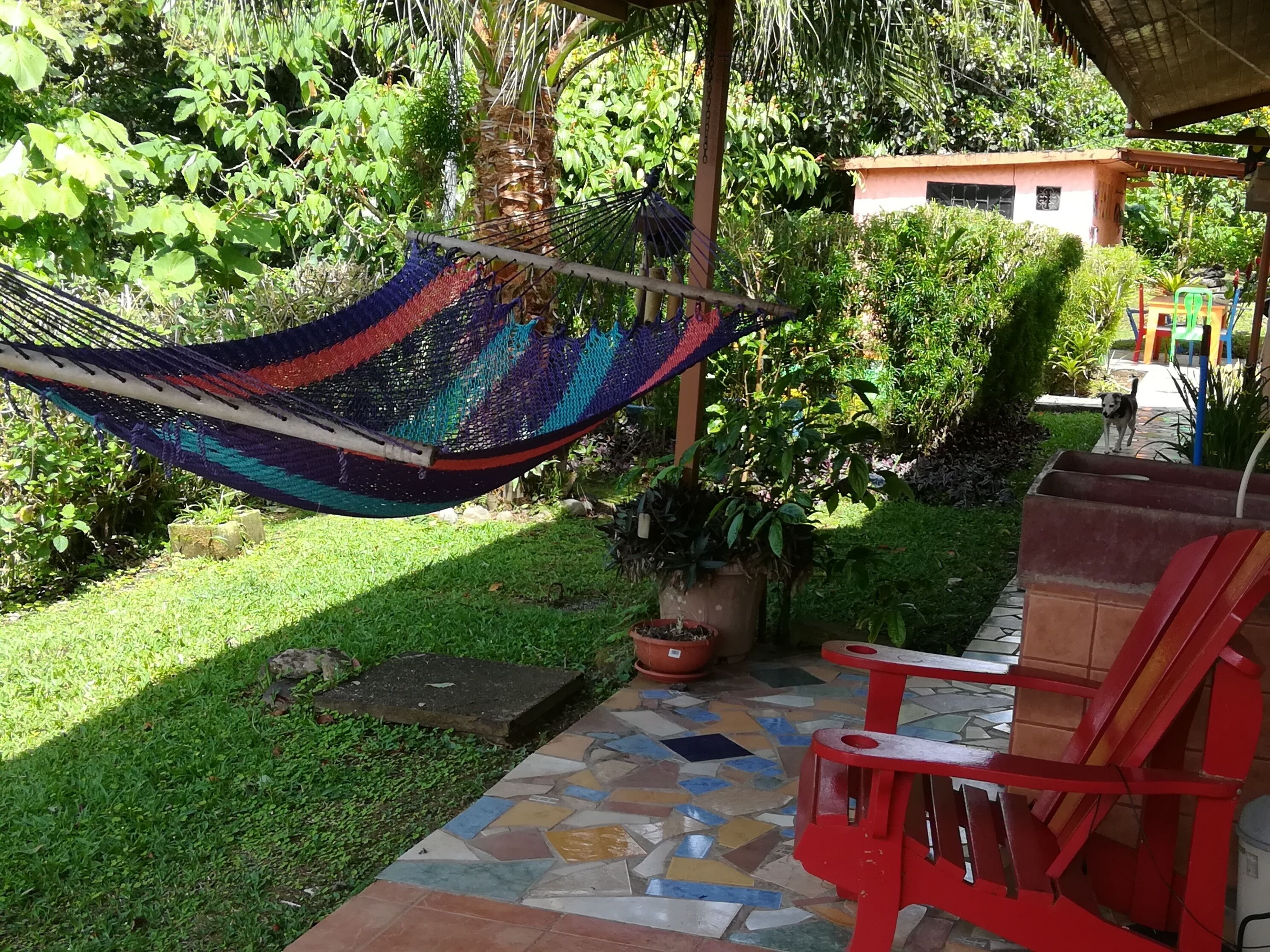 A hammock hanging between trees, a patio with a tiled floor, and a red chair.
