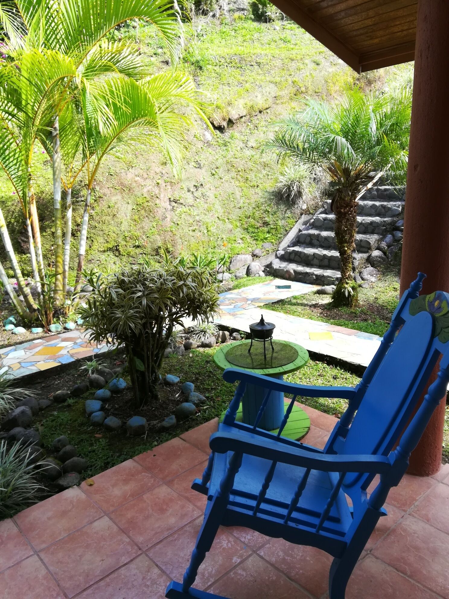 A covered patio with a blue chair, a small table, and a decorative fountain.
