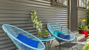 Two blue wicker chairs with cushions, a small table, and a potted plant against a corrugated metal wall. - BLUE APPLE LODGE - a fabulous mountain holiday escape! SPECIALS ON NOW ! (Bilpin)