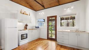 A modern kitchen with white cabinets, a wooden floor, a built-in oven, and a window with a view of greenery. - BLUE APPLE LODGE - a fabulous mountain holiday escape! SPECIALS ON NOW ! (Bilpin)