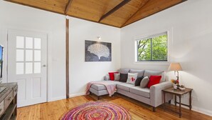 A cozy living room with a grey sofa, colorful rug, and a window with a view of greenery. - BLUE APPLE LODGE - a fabulous mountain holiday escape! SPECIALS ON NOW ! (Bilpin)
