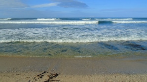 A beach with clear water and waves, sandy shore, and a clear sky.
