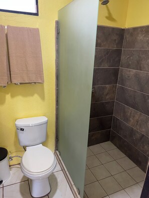 Une salle de bain avec des toilettes, un espace douche avec des carreaux foncés et un mur jaune.
