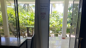A room with a table and chairs, a sign indicating checkout time, and a view of greenery outside.