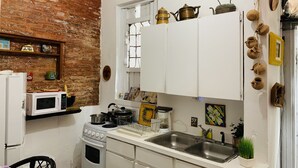 Une cuisine de taille réduite avec des meubles blancs, un mur en briques, un four à micro-ondes, une cuisinière et divers ustensiles de cuisine.
