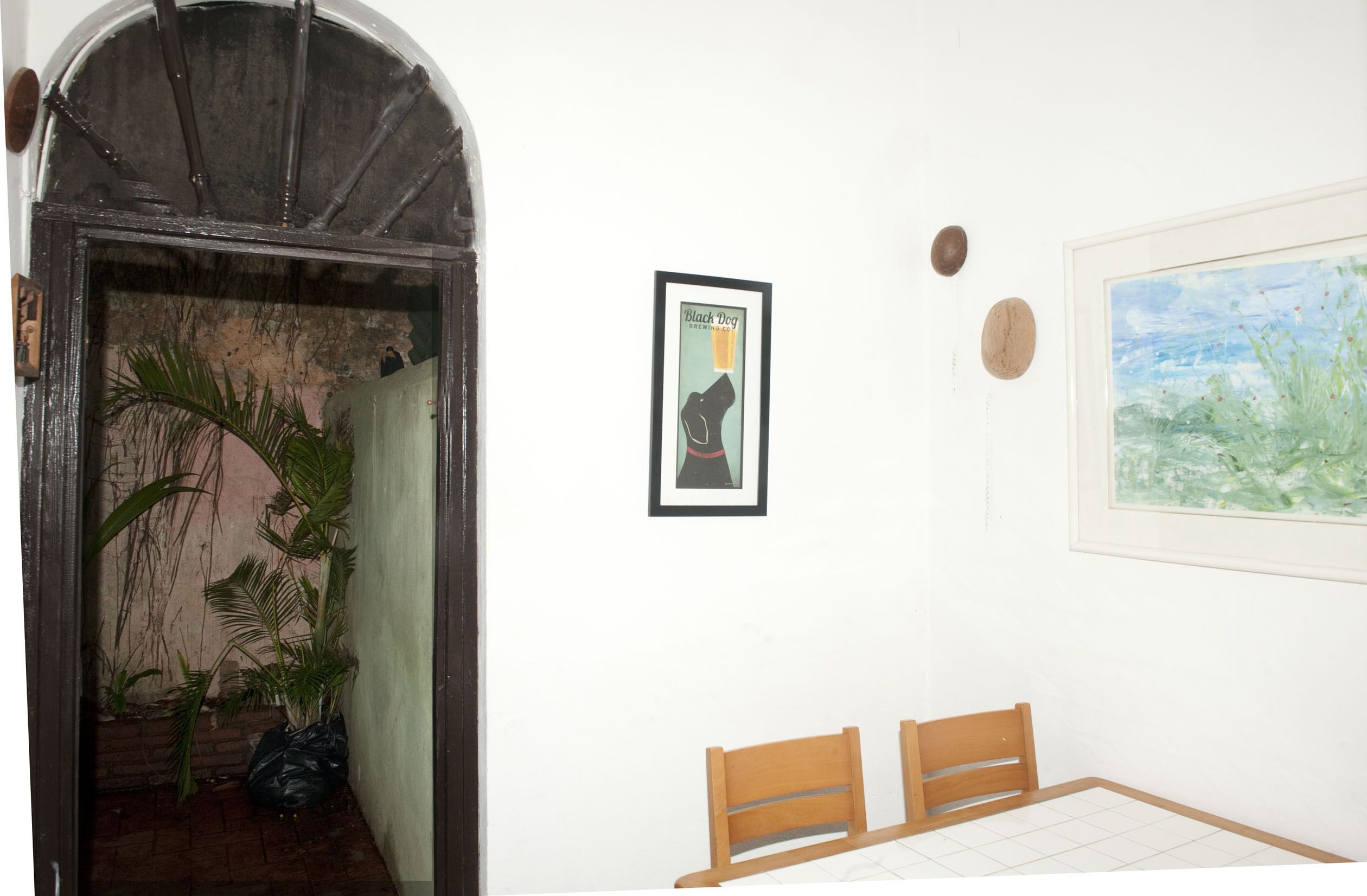 A room with a wooden door, a framed poster, a painting, and a small table with chairs.