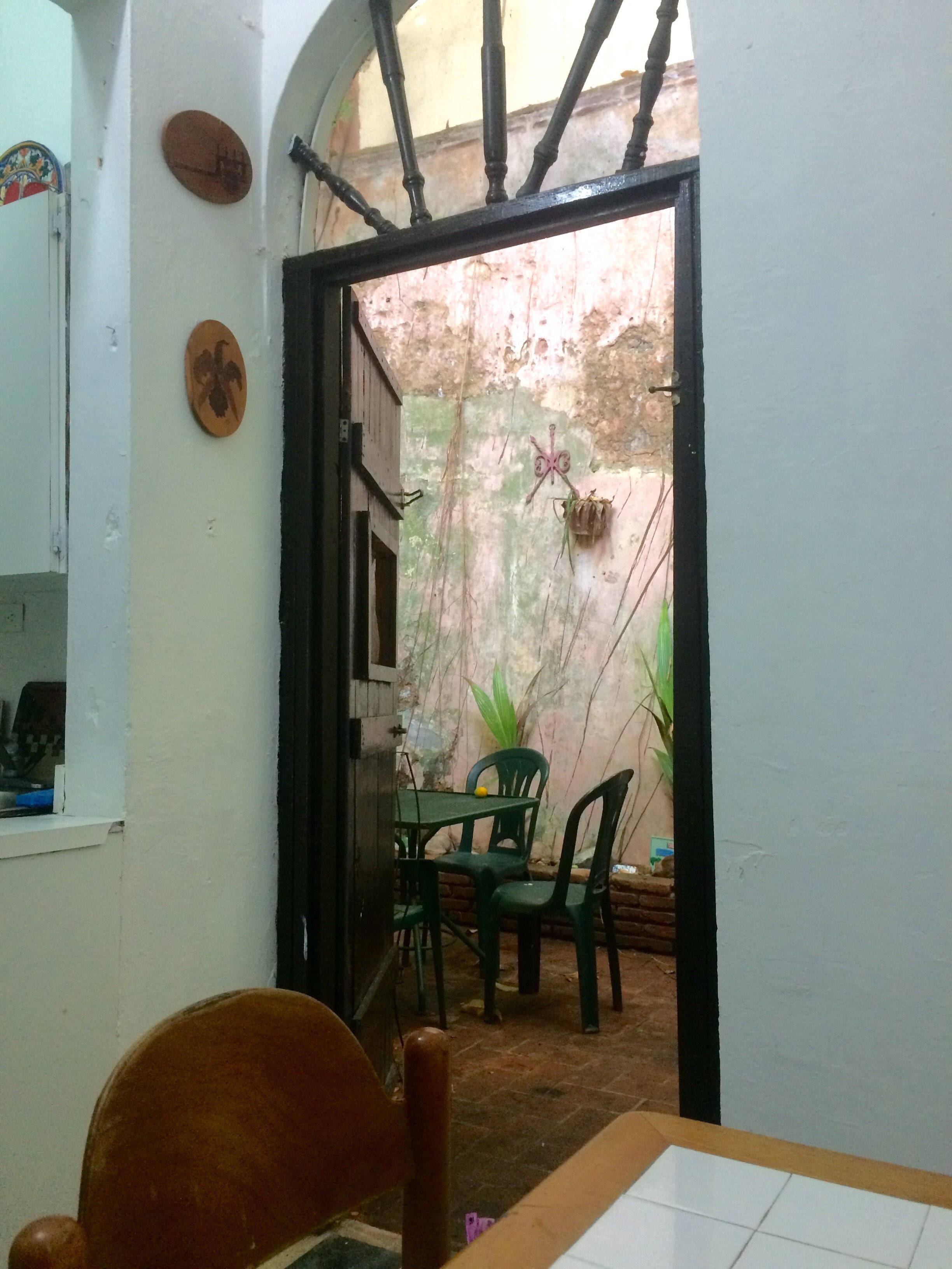 A small, enclosed patio area with a table and chairs, a hanging plant, and a rustic wall.